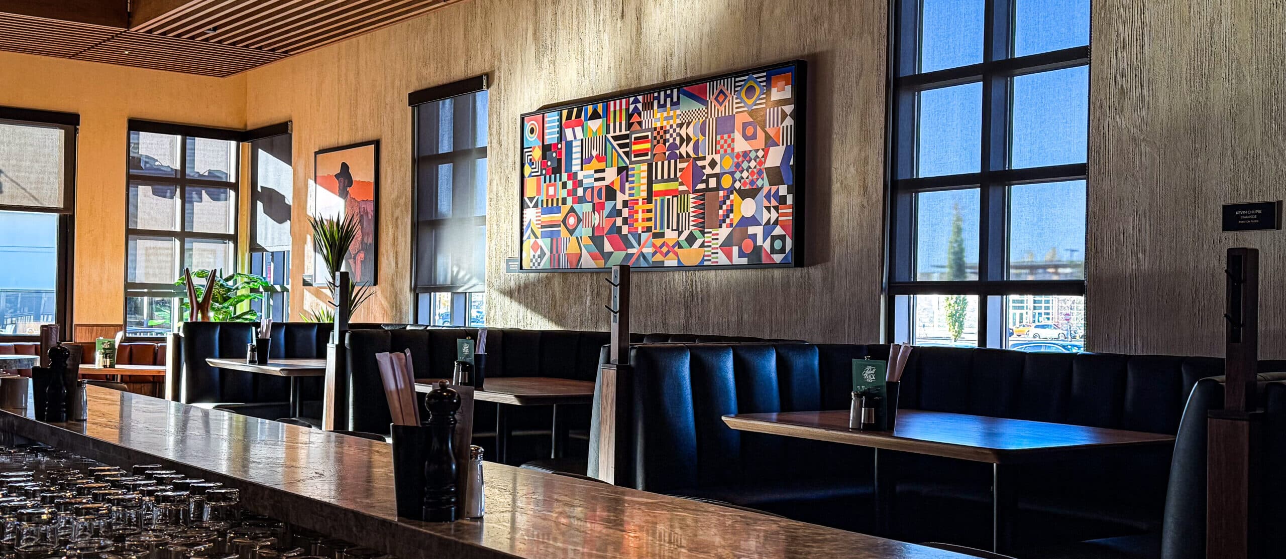 Restaurant interior with brown and black leather booths, a decorative plant, and modern art on the walls.